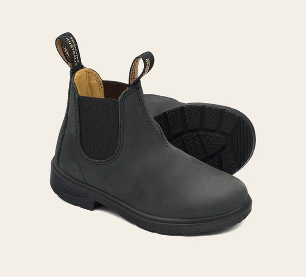 A pair of kids' Blundstone boots in rustic black color, featuring a slip-on design with elastic side panels, a round toe, and a flat polyurethane sole.